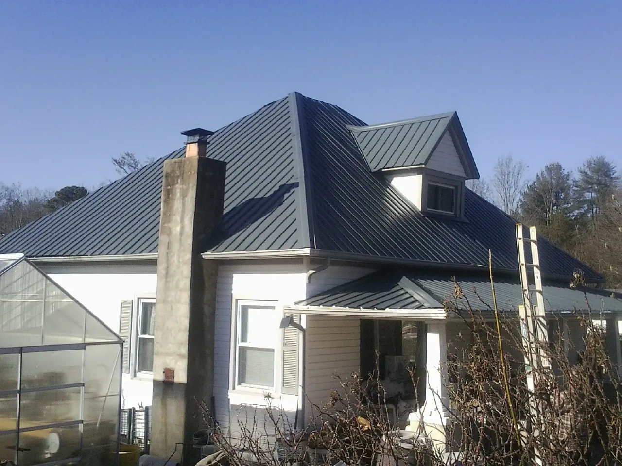 Dark blue standing seam metal roof on a white farmhouse with dormer — Slate & Tile Roof Repair by Roofing Brothers in Morenci