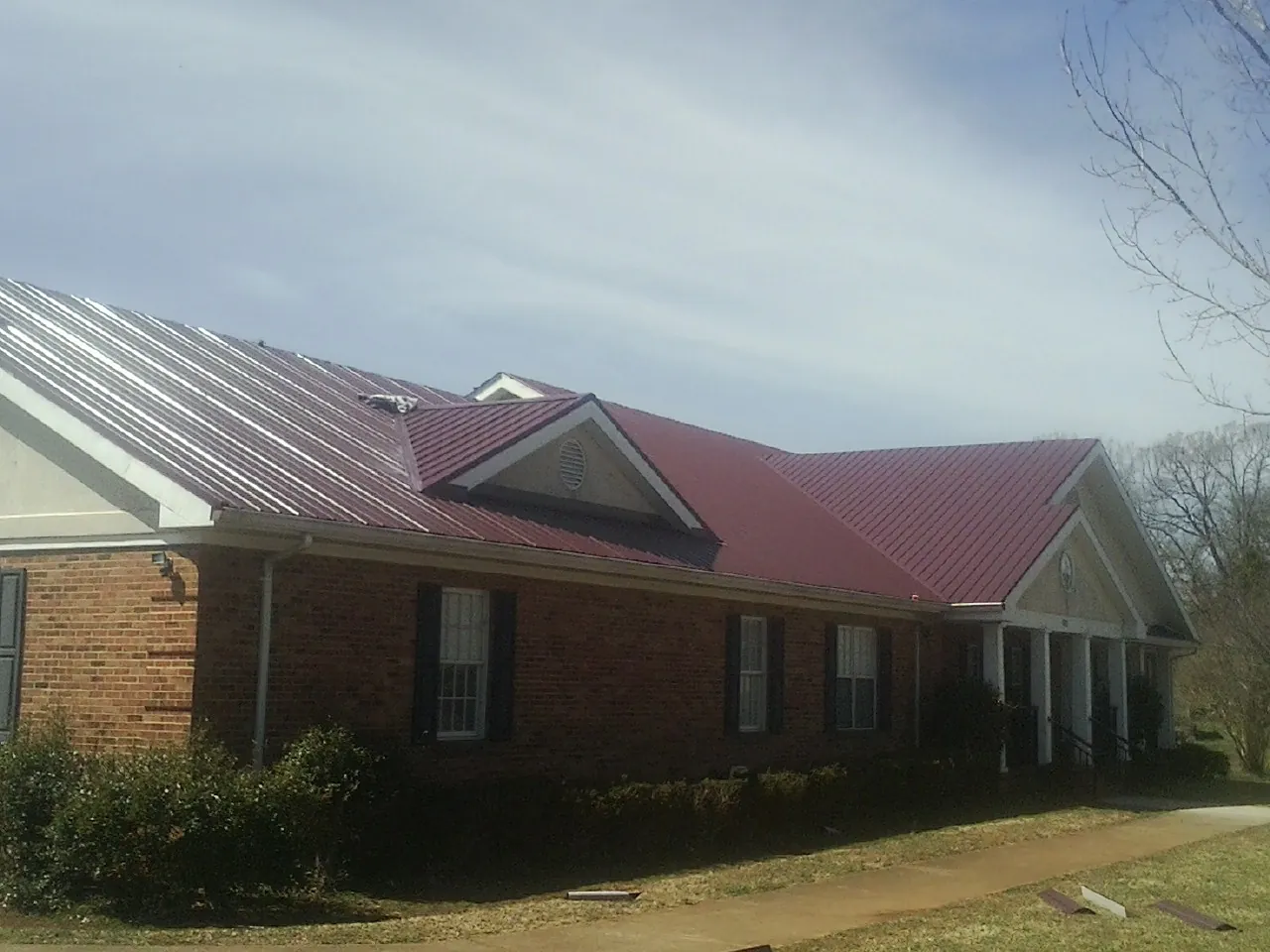 Red metal roof with gabled entries on a long brick building, from a Hail Damage Roof Repair job in Morenci