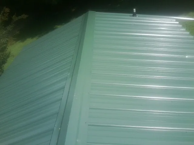 New green metal panels meeting at the ridge of a roof — Flat Roof Repair work by our crew in Morenci