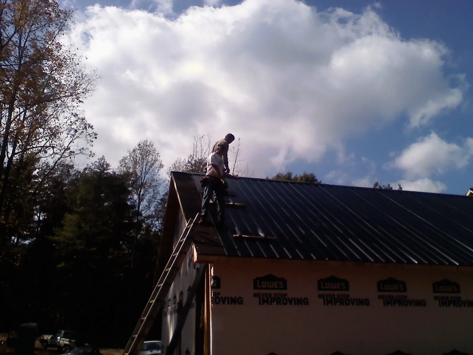 Roofer fastening dark metal panels high against a cloudy sky, from a Roof Inspection job in Morenci