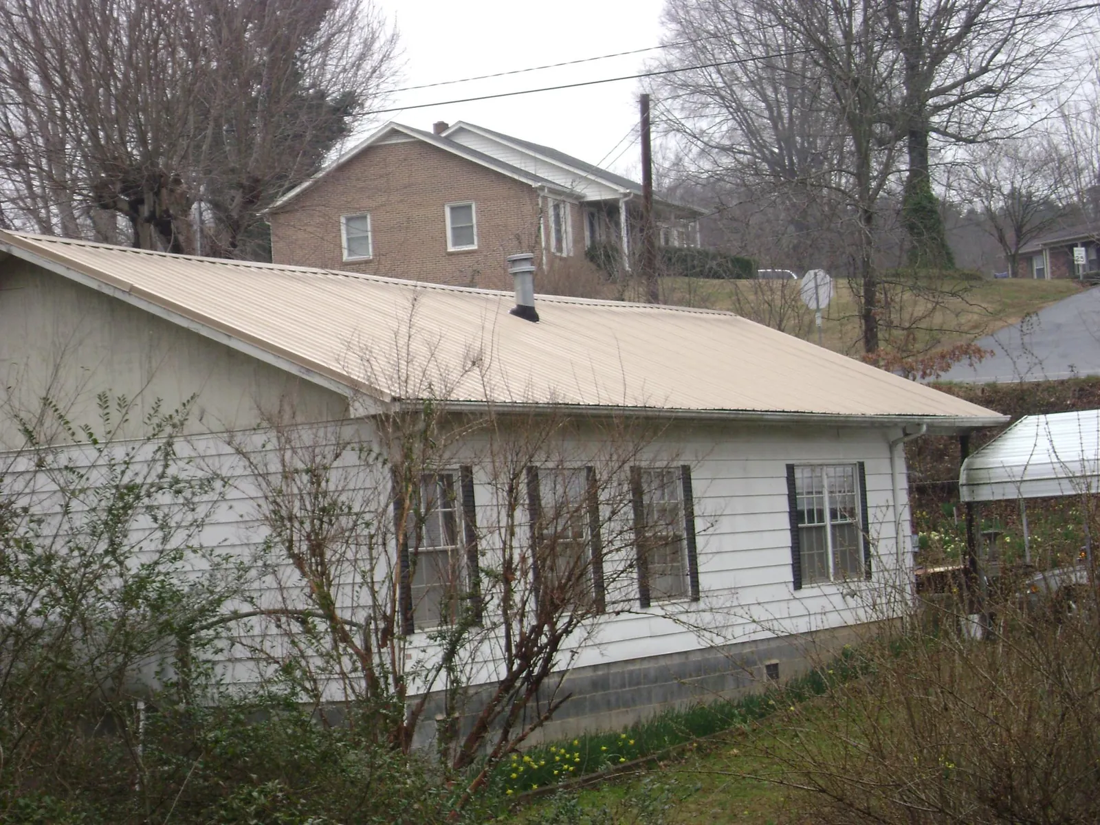 Tan metal roof on a white sided house set into a hillside — Commercial Roofing by Roofing Brothers in Morenci