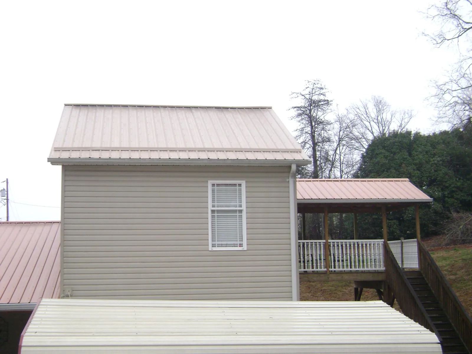 Tan metal roofs on a two story addition and attached porch, from a Roof Replacement job in Morenci